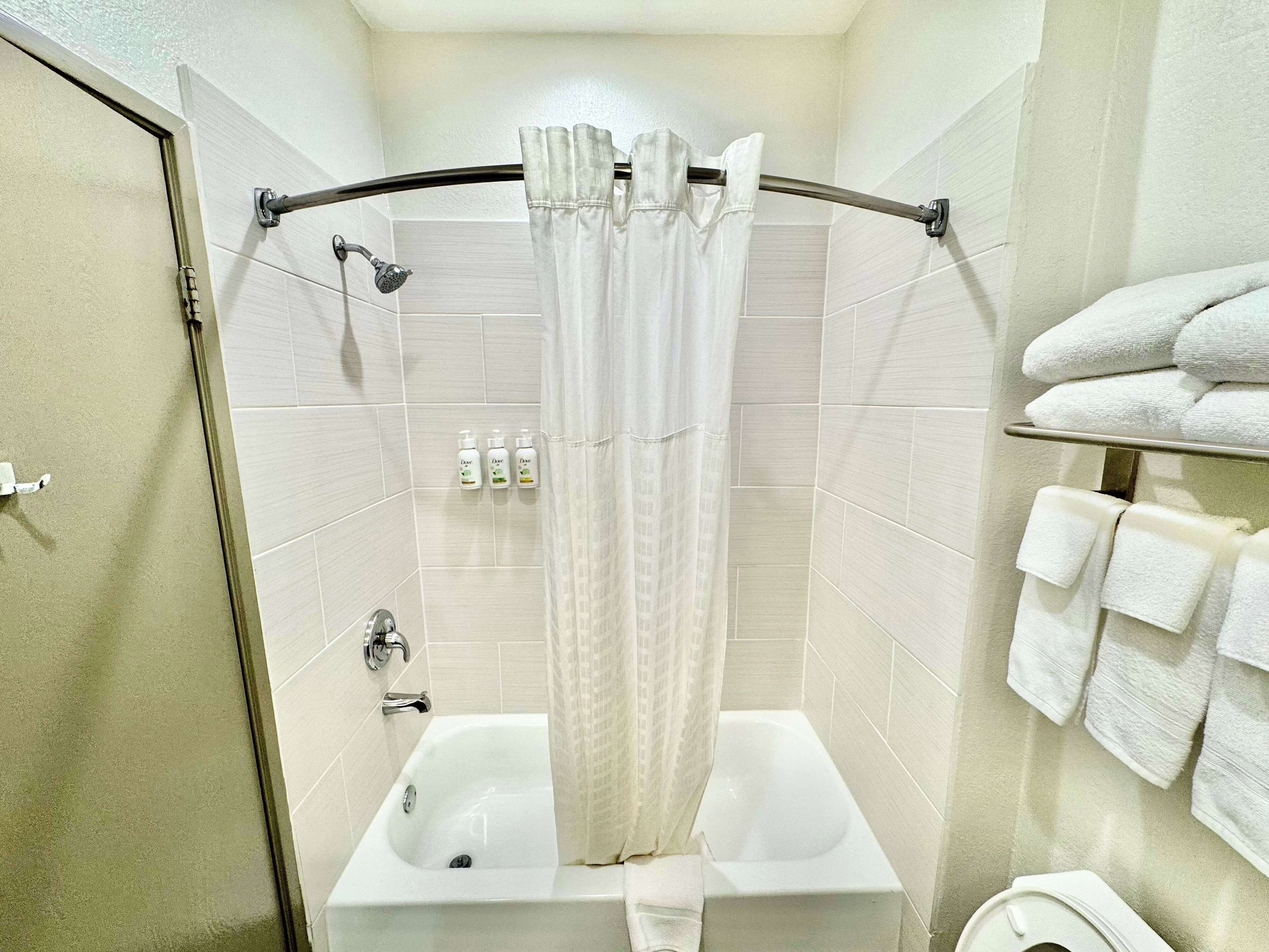 Een badkamer met een bad, douchegordijn, toilet en een handdoekrek met handdoeken.