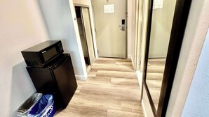 Un couloir étroit, avec un micro-ondes et une poubelle sur le côté gauche, mène à une porte sur laquelle est apposée une pancarte.