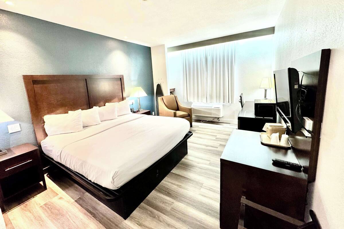 A hotel room with a large bed, a desk with a computer, a chair, and a TV.