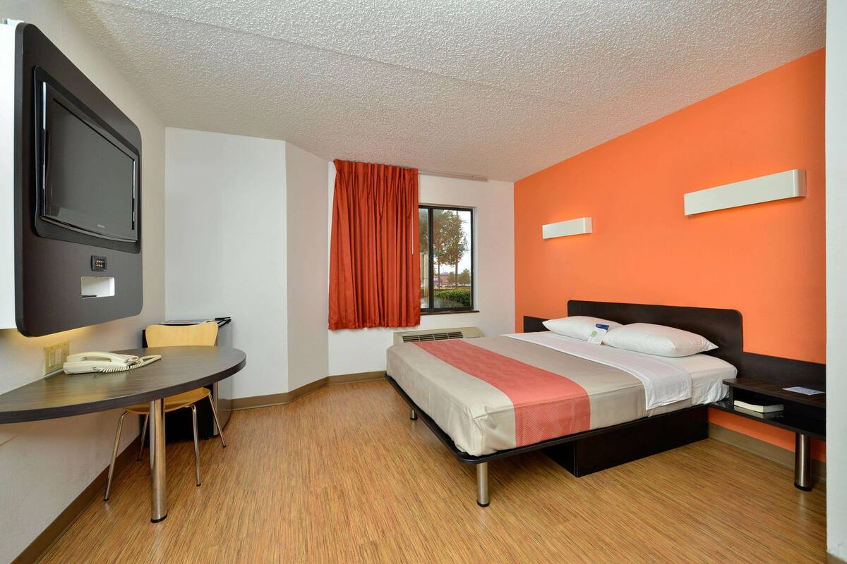 A hotel room with a bed, a desk, a chair, a TV, and a window with curtains.