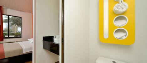 Una habitación de hotel con cama, ventana y baño que incluye inodoro y toallero.