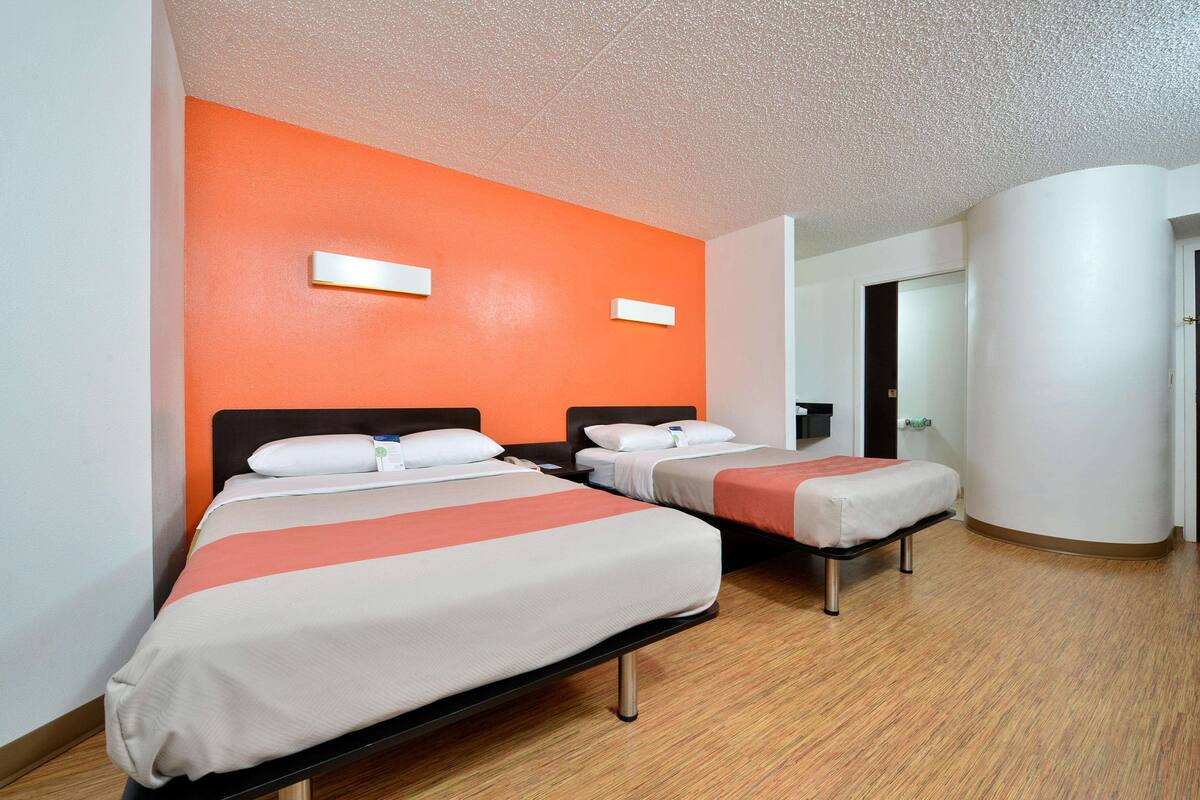 A hotel room with two beds, a wooden floor, and an orange accent wall.