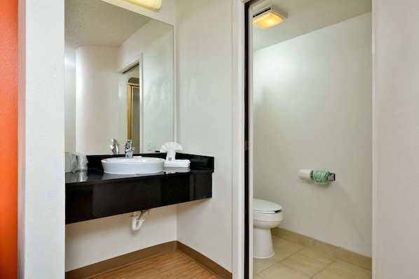 A bathroom with a black countertop sink, a mirror, and a toilet. - Motel 6 Plano, TX - West - Frisco (Plano)