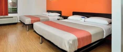 Habitación de hotel con dos camas, una ventana con cortinas rojas y una pared de acento anaranjada.