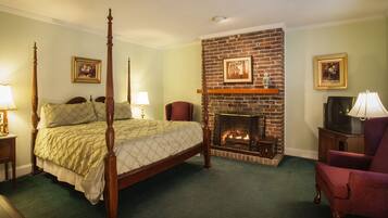 A four-poster bed with a quilt, a brick fireplace, a television, and a red armchair in a hotel room.