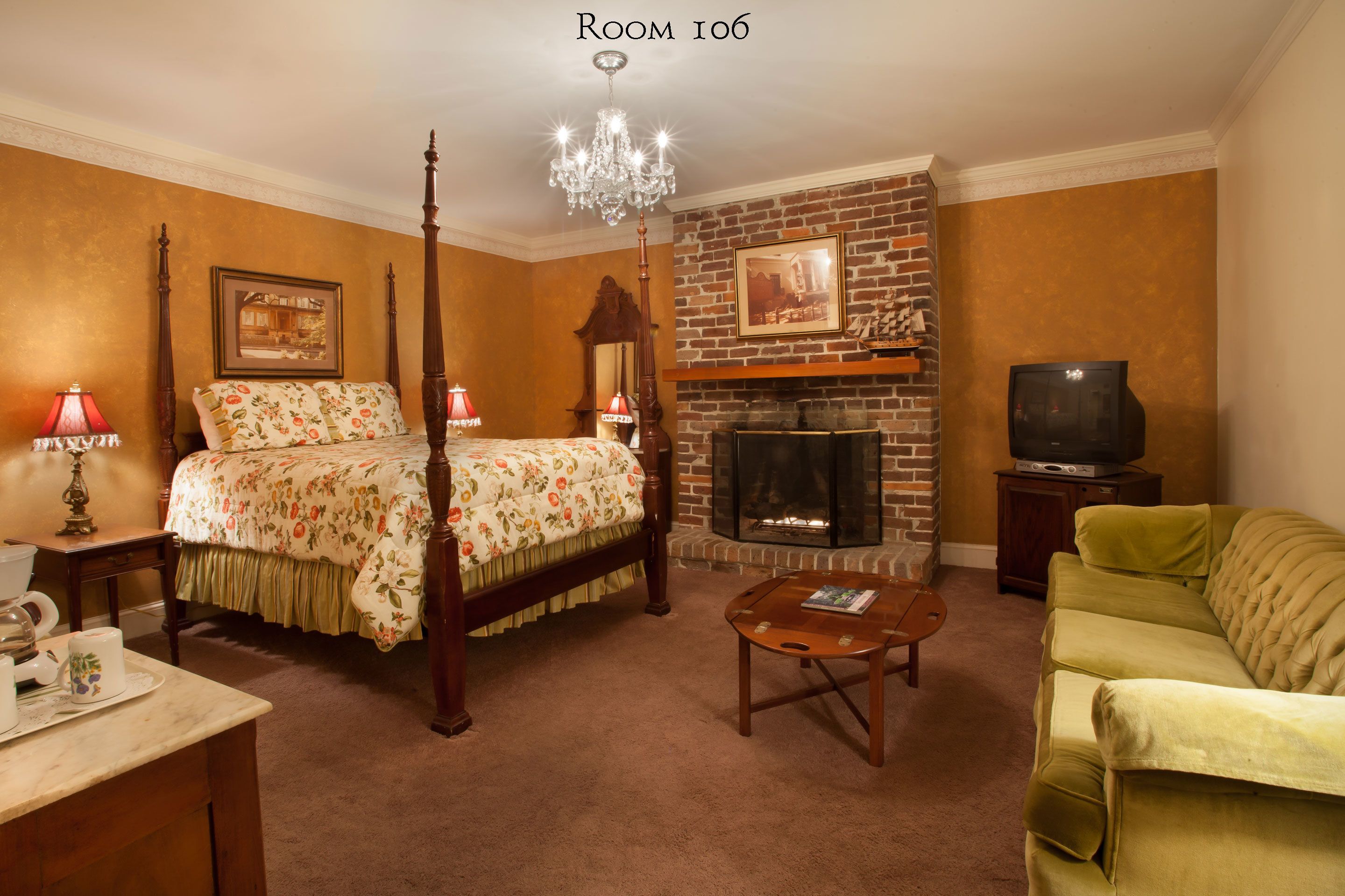 A room with a four-poster bed, a fireplace, a television, and a green armchair.