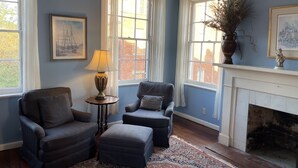 A room with two armchairs, a small table with a lamp, a fireplace, and large windows with curtains. - 17Hundred90 Inn and Restaurant (Savannah)