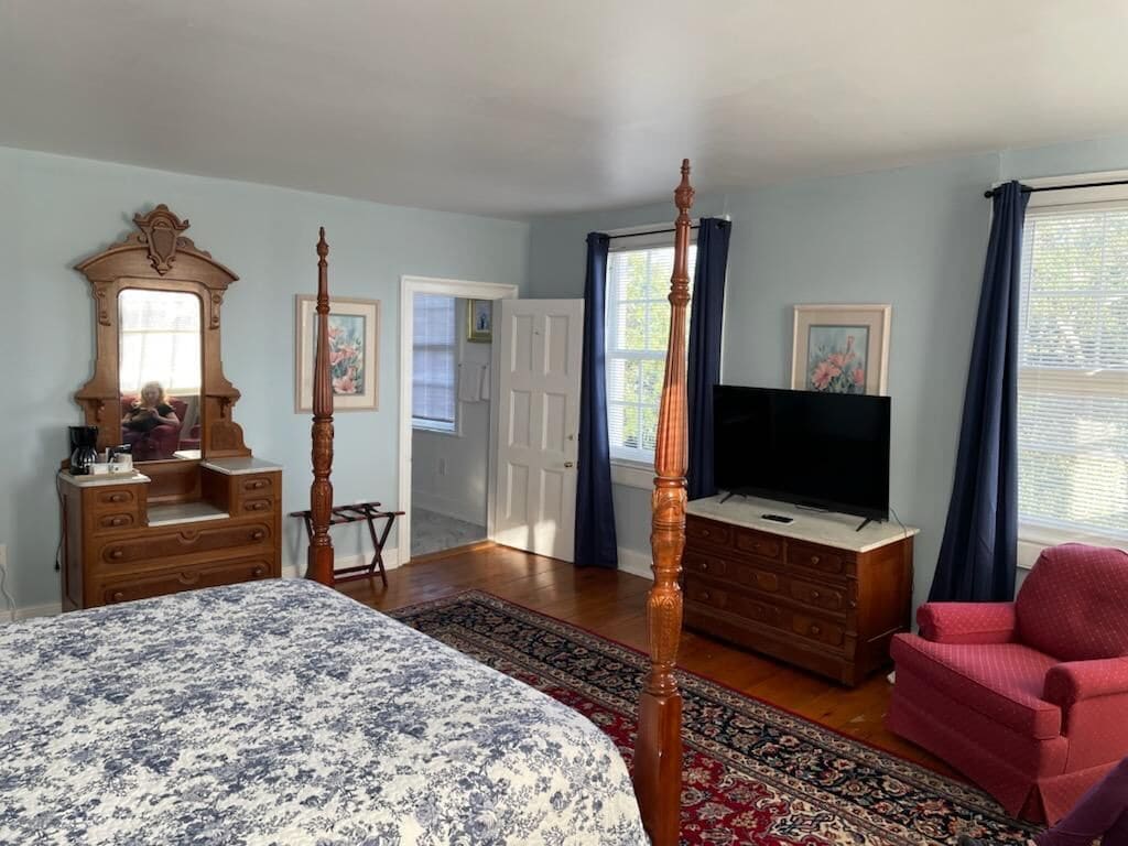 A bedroom with a four-poster bed, a dresser, a television, and a red armchair.