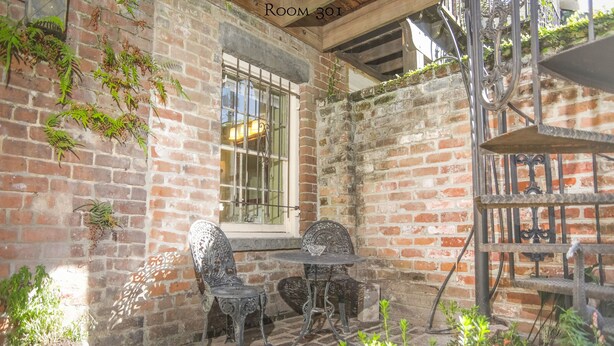 A room with brick walls, a window with bars, two metal chairs, a small table, and a metal shelf with plants. - 17Hundred90 Inn and Restaurant (Savannah)