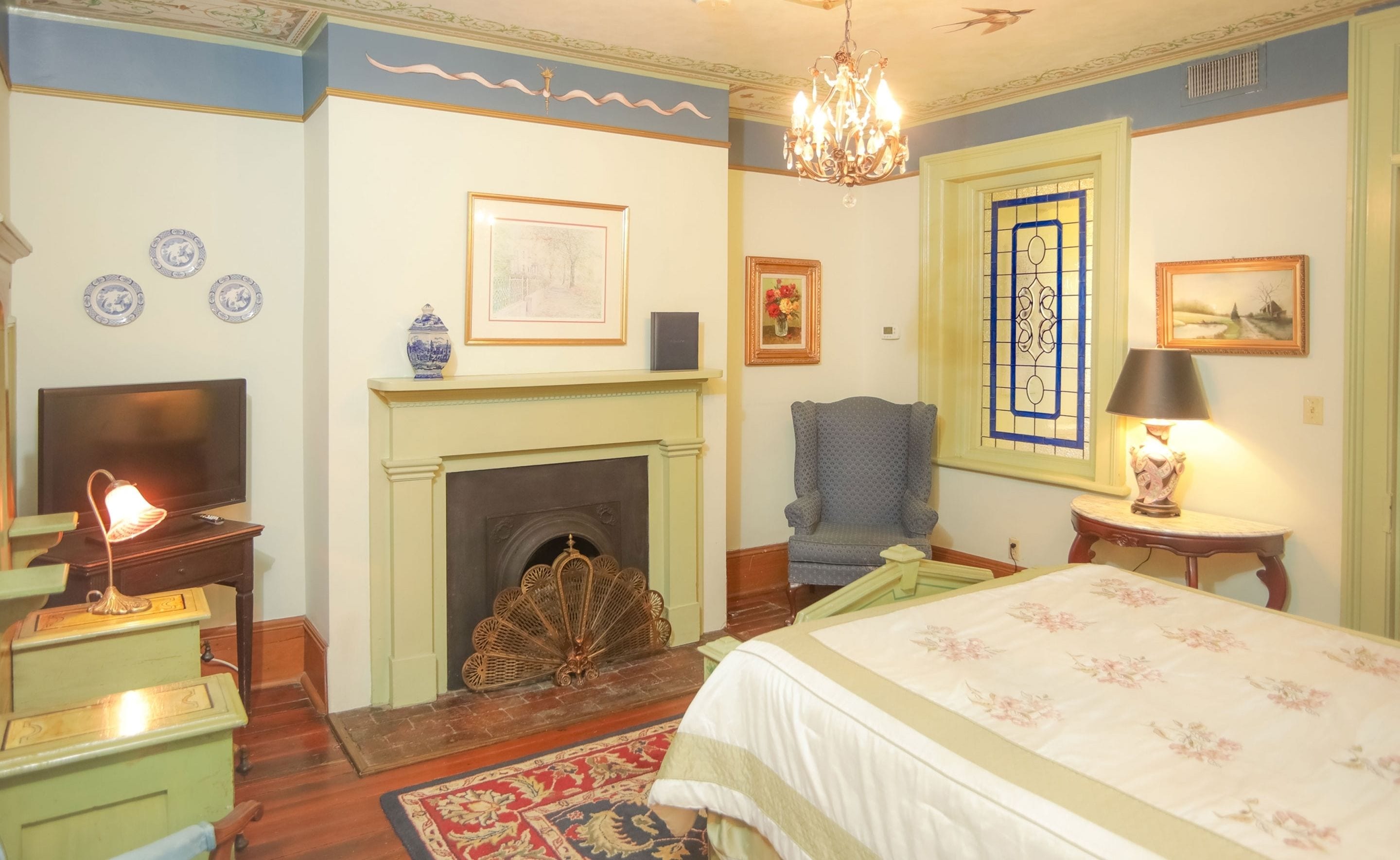 A traditional room with a fireplace, a television, a bed, and a chandelier.