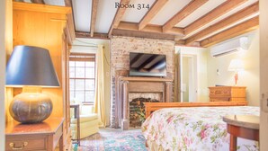 A cozy room with a fireplace, a bed with floral bedding, a wooden desk with a lamp, and a television mounted above the fireplace. - 17Hundred90 Inn and Restaurant (Savannah)