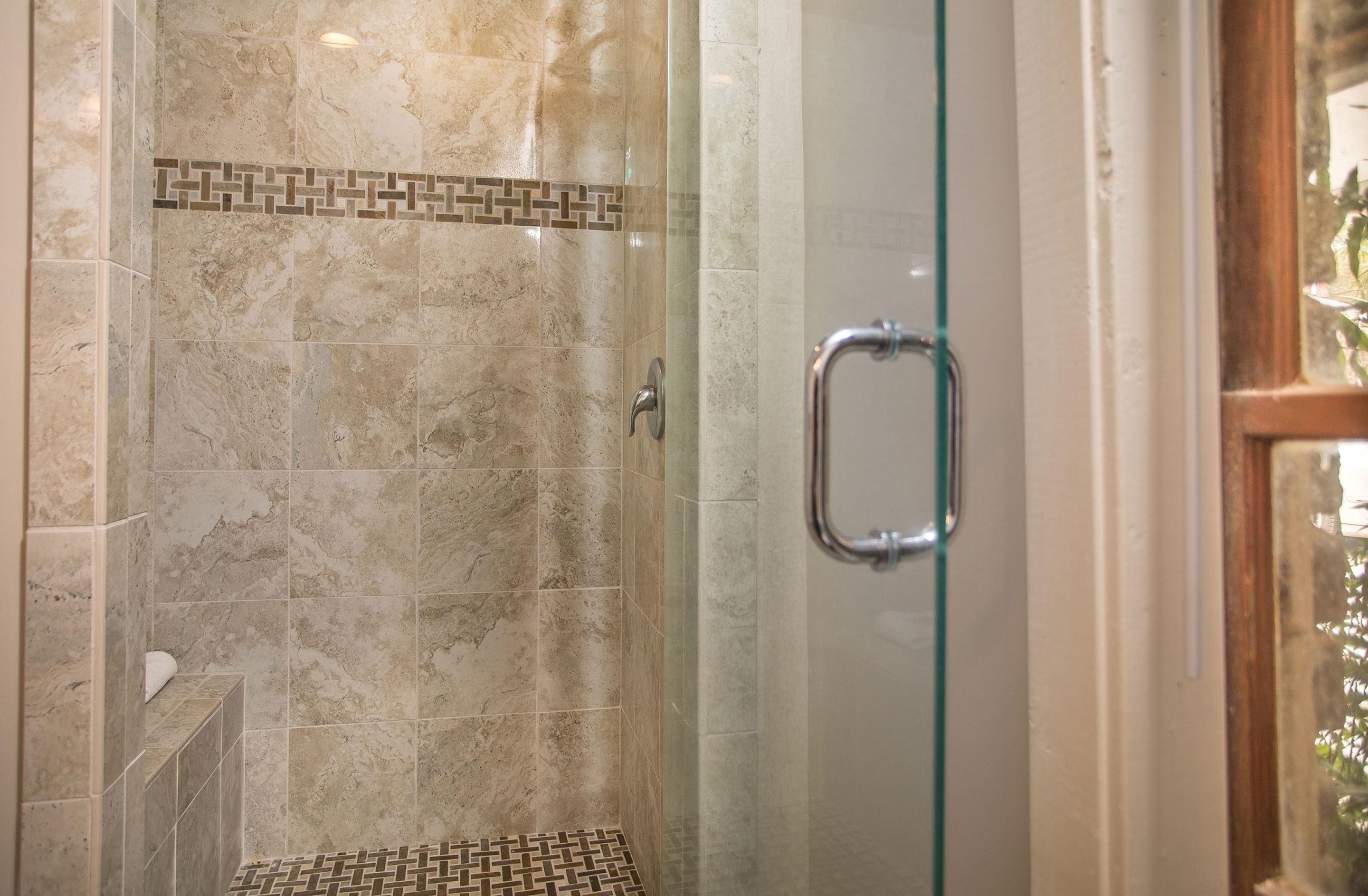 A glass-enclosed shower with a marble tile design and a metal handle.
