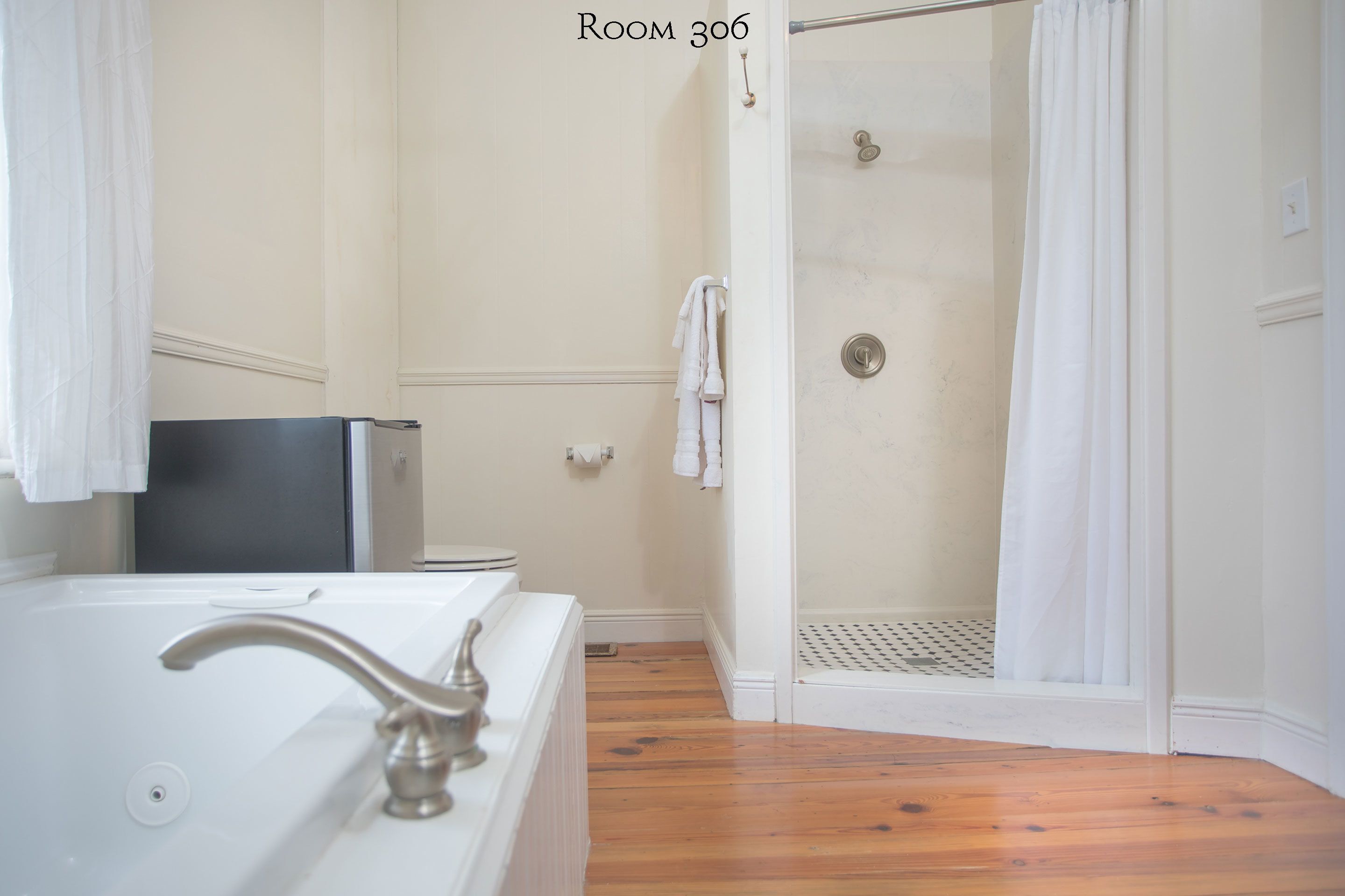 Ein Badezimmer mit Badewanne, Dusche mit Glastür und Holzboden.