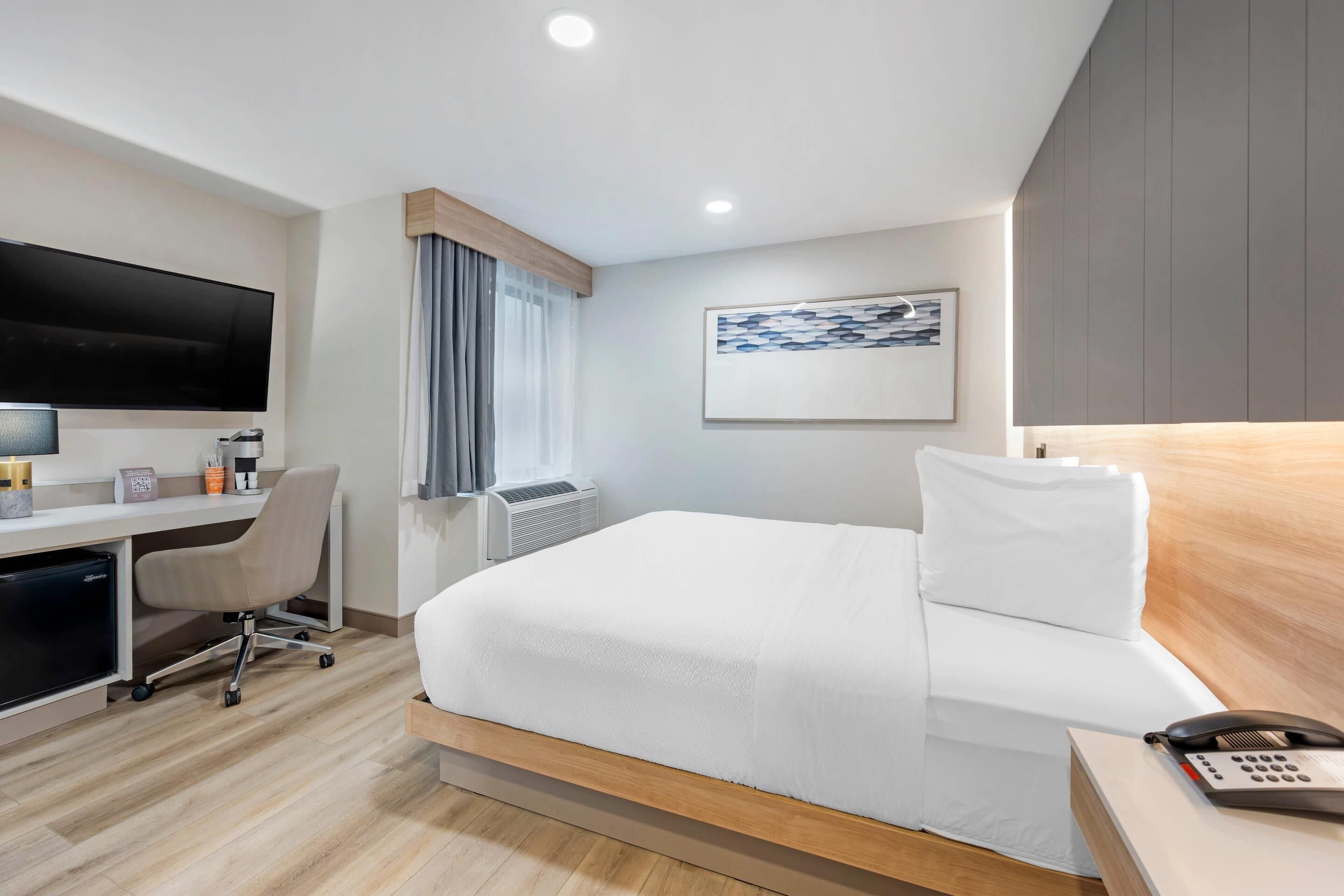 Una habitación de hotel con una cama, un escritorio con computadora, un teléfono y un televisor montado en la pared.