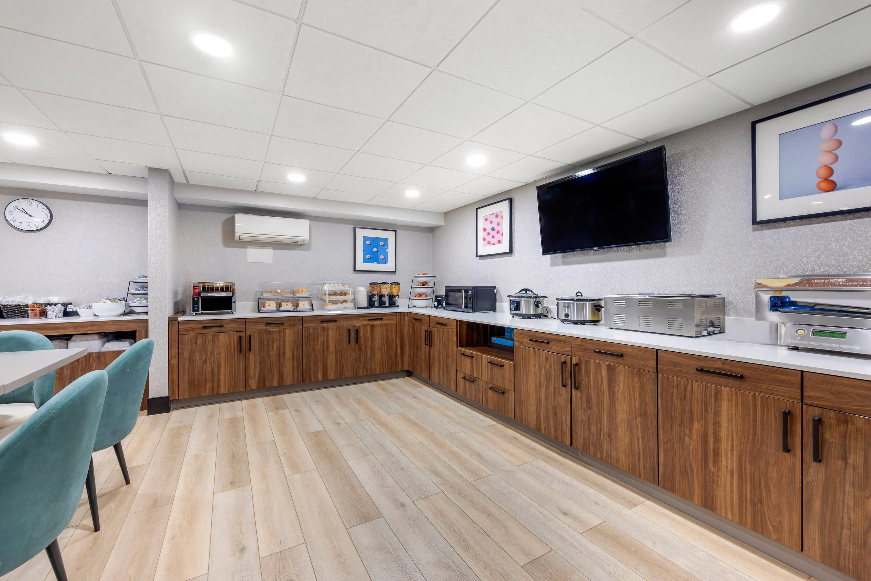 A modern kitchen with wooden cabinets, a microwave, toaster, and a flat-screen TV mounted on the wall.