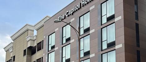 Ein mehrstöckiges Hotelgebäude mit moderner Fassade, großen Fenstern und einer auffälligen Schrifttafel mit der Aufschrift 'The Capitol Hotel'.