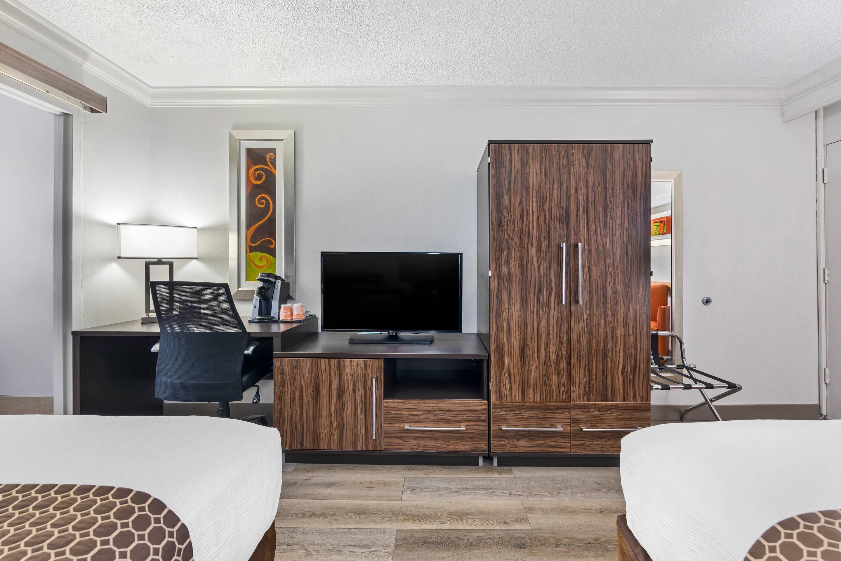 A hotel room with two beds, a desk with a TV, a wardrobe, and a chair.