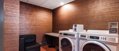 A laundry room with a front-loading washer and dryer, a black sofa, and a wooden wall.