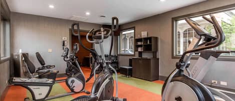 Ein Fitnesscenter mit verschiedenen Trainingsgeräten, einer Rezeption und Blick ins Freie.