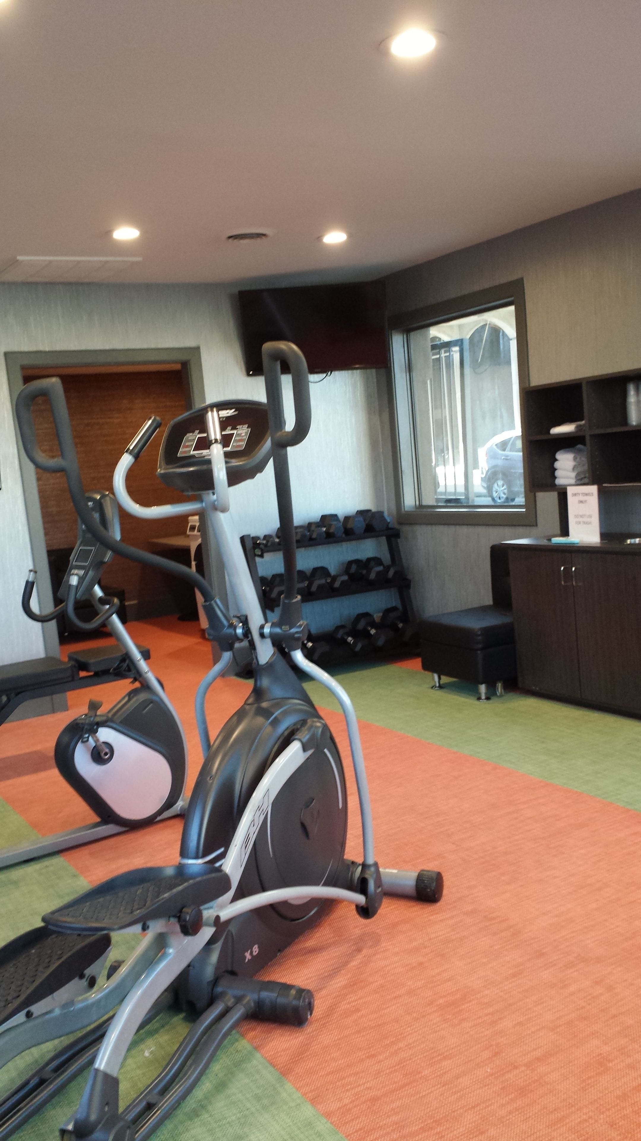 An exercise area with cardio machines, dumbbells, and a bench.