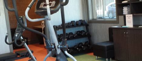 An exercise area with cardio machines, dumbbells, and a bench.