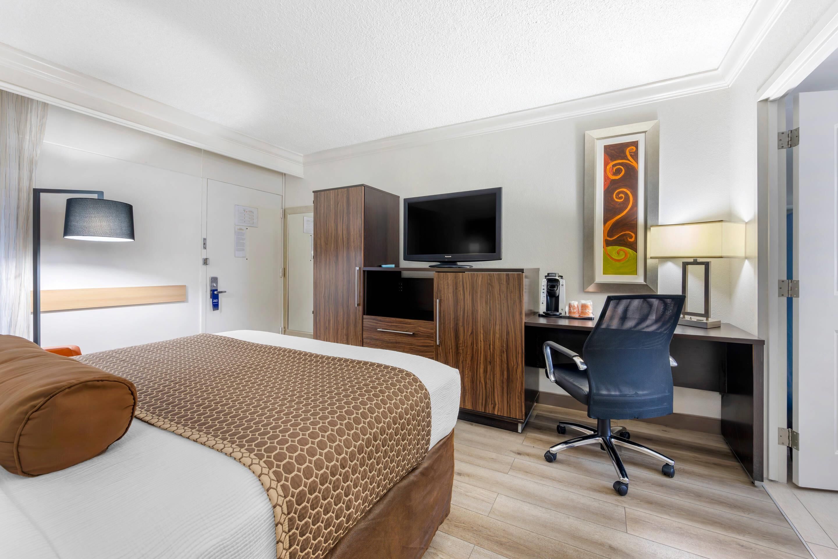 A hotel room with a bed, a desk with a computer, a television, and a chair.