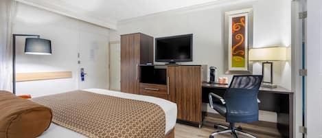 A hotel room with a bed, a desk with a computer, a television, and a chair.