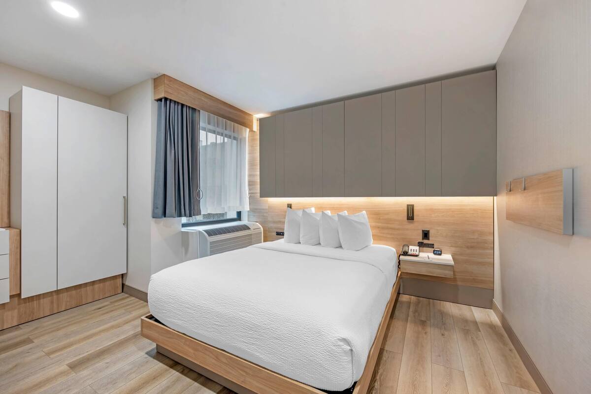 A modern hotel room with a large bed, a bedside table, a wardrobe, and a window with curtains.