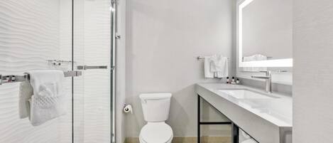 Un baño moderno con cabina de ducha de vidrio, inodoro, lavamanos y un espejo grande.