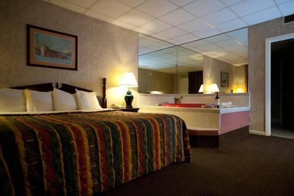 A hotel room with a bed, a bedside table, a mirror, and a bathroom visible through an open door.