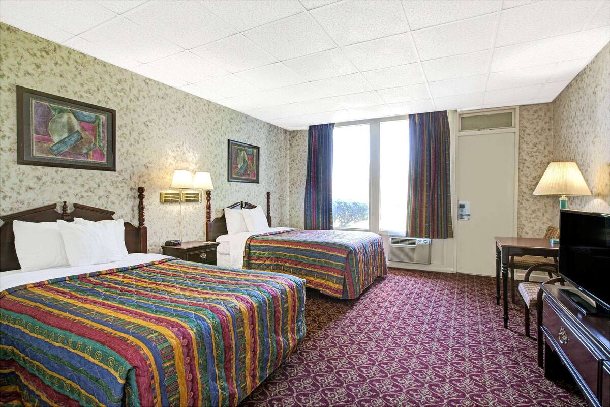 A hotel room with two beds, a TV, a desk, and a window with curtains.