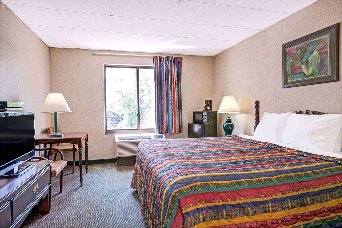 A hotel room with a large bed, a desk, a television, and a window with curtains.