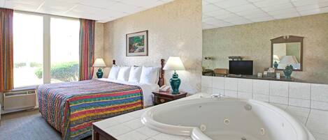 A hotel room with a large bed, a bathtub, a desk with a lamp, and a television.