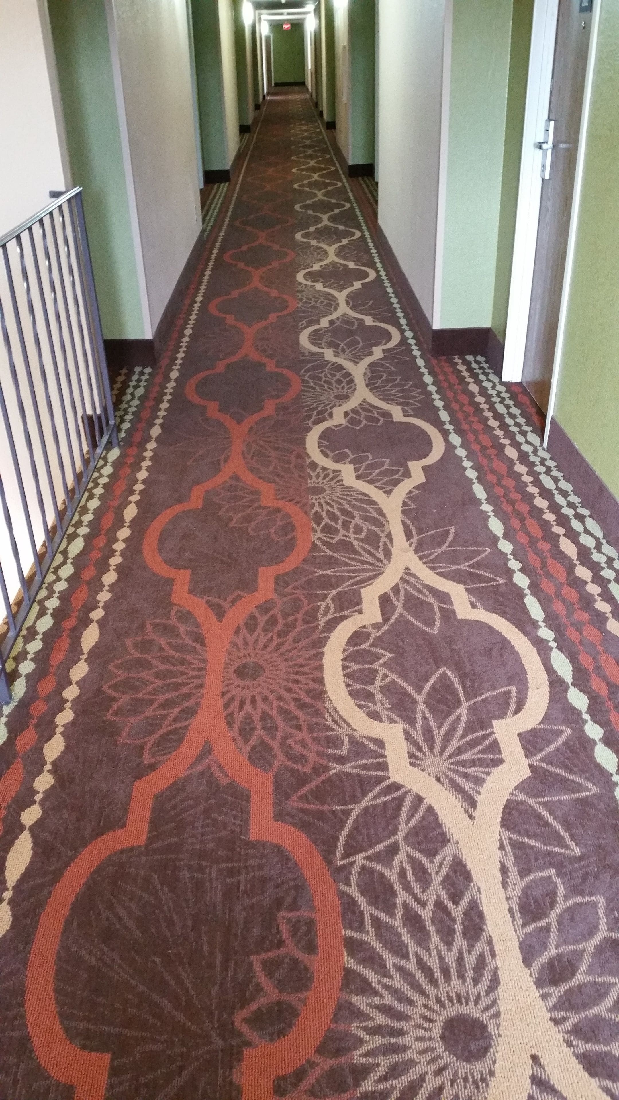 A long hallway with a patterned carpet and a metal railing on one side.
