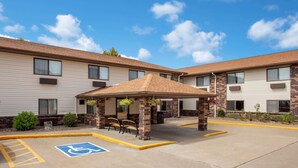 Un área de estar al aire libre techada con un espacio de estacionamiento para discapacitados frente a un motel con fachada de ladrillo y revestimiento.
