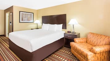 A hotel room with a large bed, two bedside tables with lamps, a patterned armchair, and a framed picture on the wall.