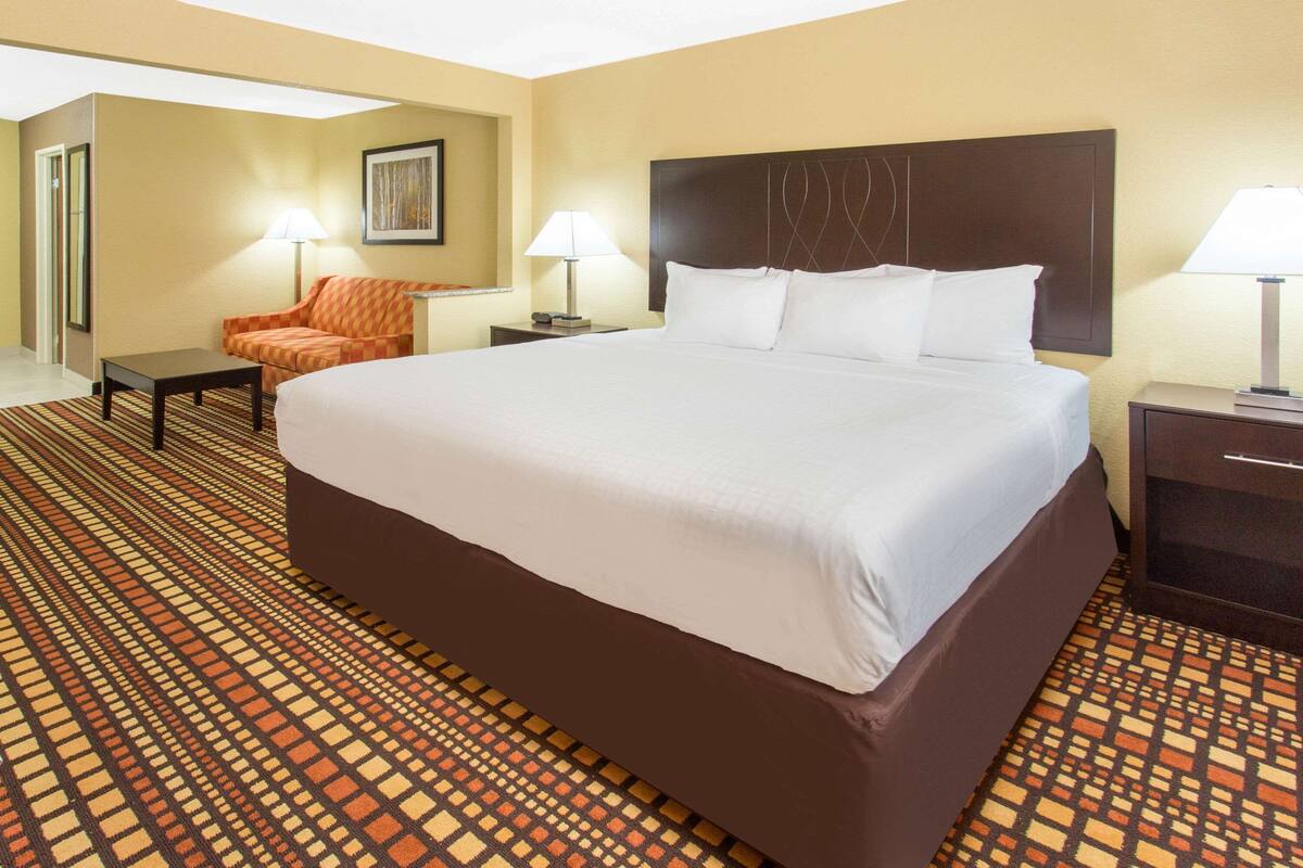 A hotel room with a large bed, two bedside tables with lamps, a chair, and a patterned carpet.