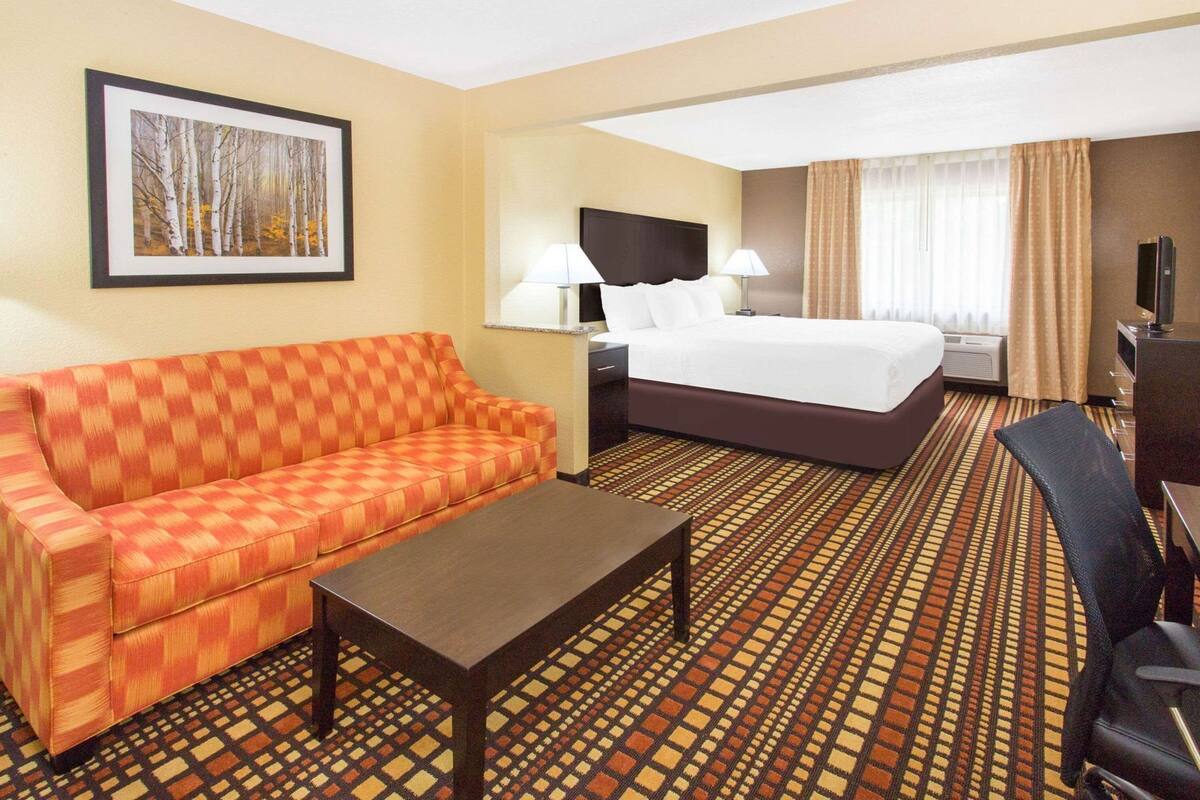 A hotel room with a bed, a sofa, a coffee table, a TV, and a painting on the wall.