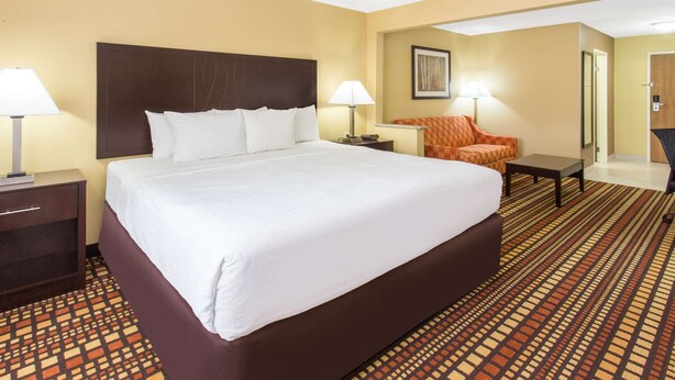 Una habitación de hotel con una cama grande, dos mesitas de noche, una silla, un escritorio y un espejo.