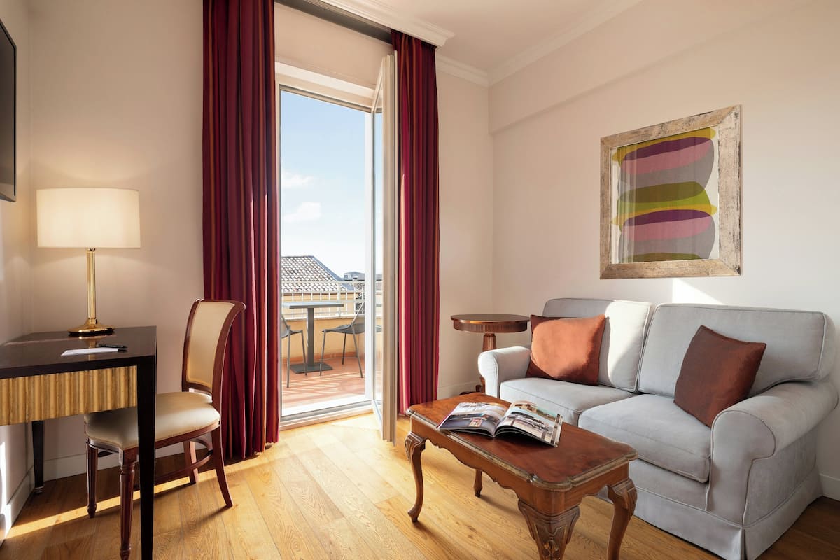 A room with a sofa, a chair, a table, a lamp, and a window with curtains.