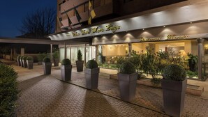 A hotel entrance with a modern facade, large potted plants, and a well-lit entrance area. - Sina Maria Luigia (Parma)