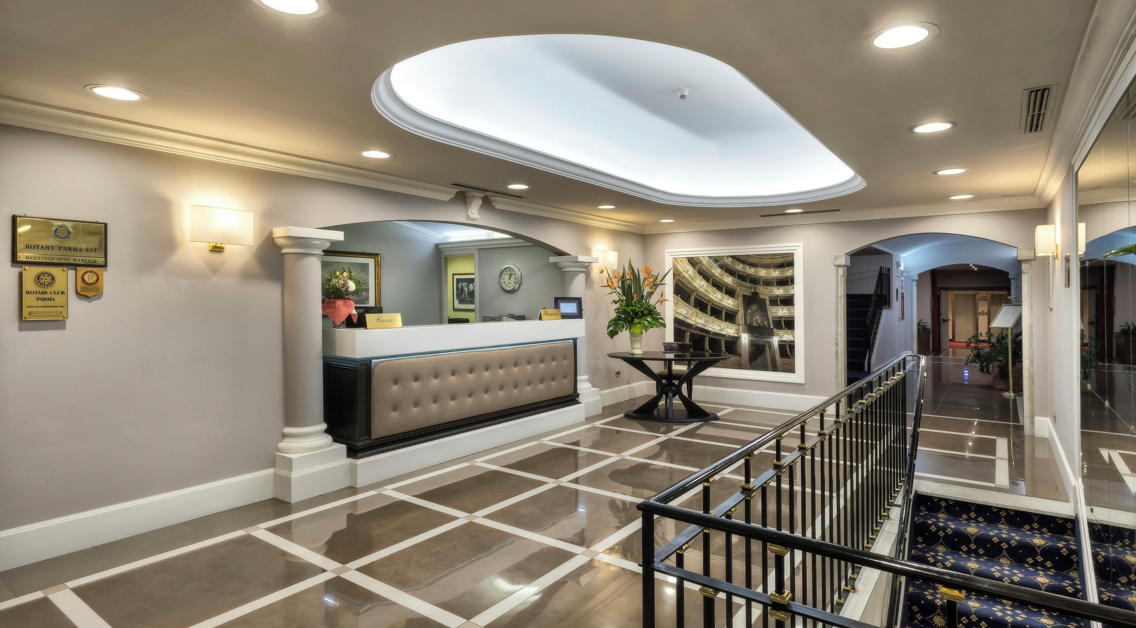 Una hall d'albergo con la reception, una sveglia, uno specchio decorativo e una scalinata.