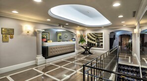 Un vestíbulo de hotel con una recepción, un reloj, un espejo decorativo y una escalera.
