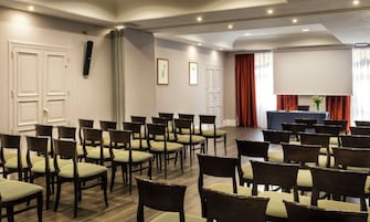 Un salón de conferencias con filas de sillas, una pantalla de proyector y una mesa con un micrófono.