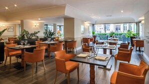 A spacious restaurant with multiple tables and chairs, large windows, and indoor plants. - Sina Maria Luigia (Parma)