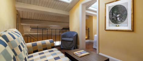 A room with a checkered sofa, a patterned armchair, a wooden coffee table, a framed artwork, and a skylight.