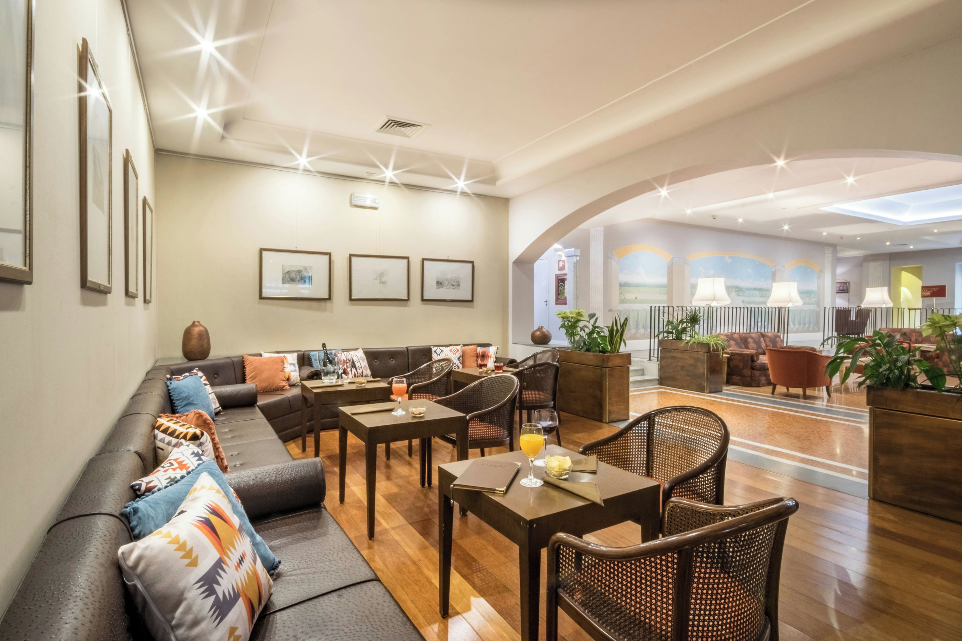 Een moderne hotelentree met een zithoek, tafels en een trap naar een hoger gelegen niveau.