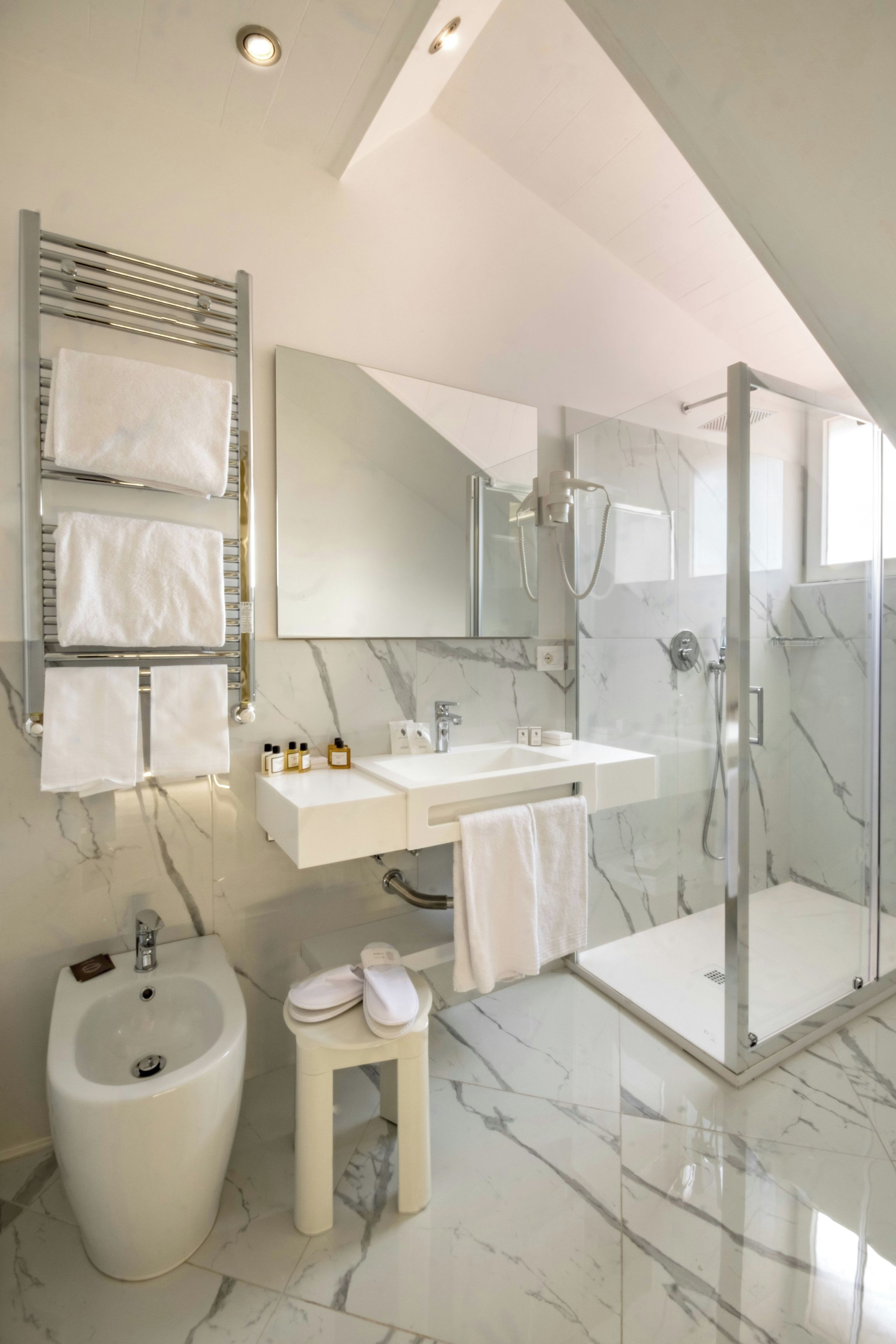 Un baño moderno con un bidé, un tocador con espejo, ducha y un taburete pequeño.