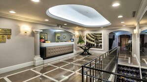 A hotel lobby with a reception desk, a clock, a decorative mirror, and a staircase. - Sina Maria Luigia (Parma)