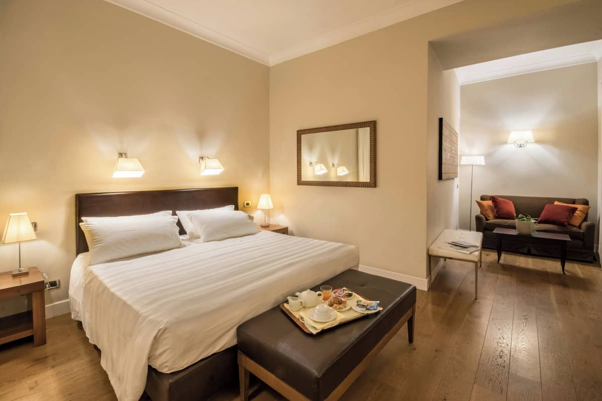 A hotel room with a bed, bedside lamps, a small table with a tray of breakfast, a sofa, and a mirror on the wall.